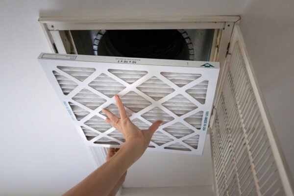 Adult white homeowner installing a new air filter in an intake vent in a home ceiling.